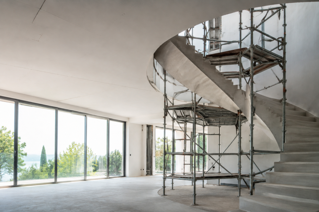Échafaudage métallique entourant un escalier tournant en béton dans une maison moderne en cours de rénovation.